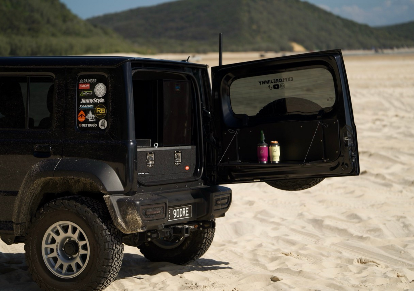 Black off-road vehicle with open rear door showcasing the jimny xl drawer system on sandy terrain